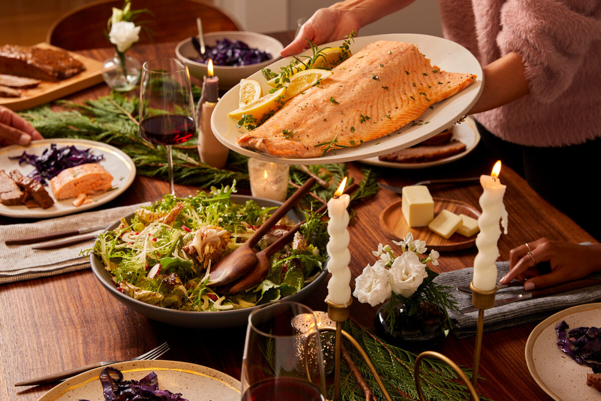 Hands serving a plate of salmon over a festive tablescape