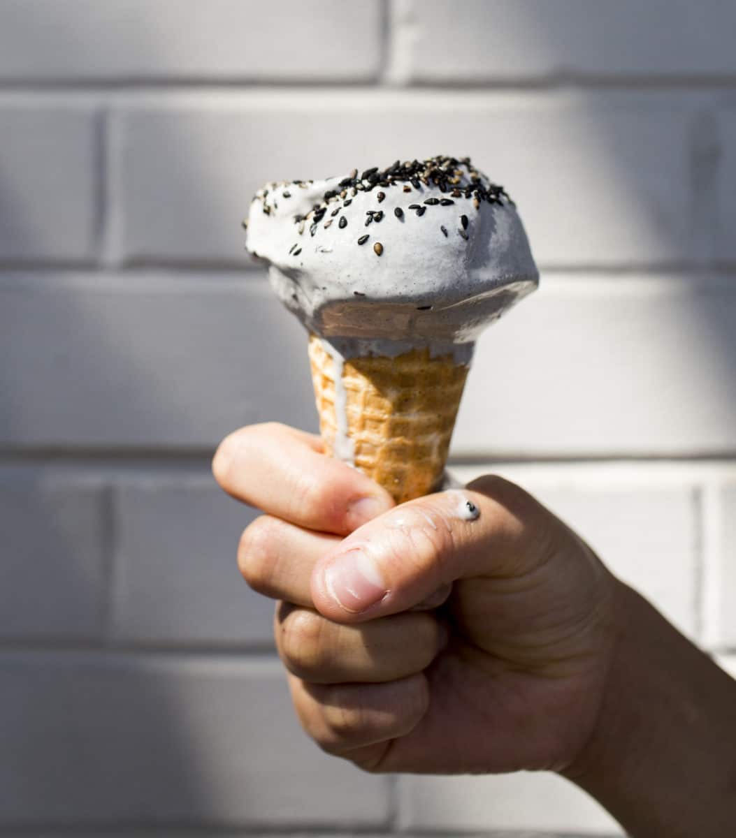 A hand holding a melting cone of black sesame ice cream