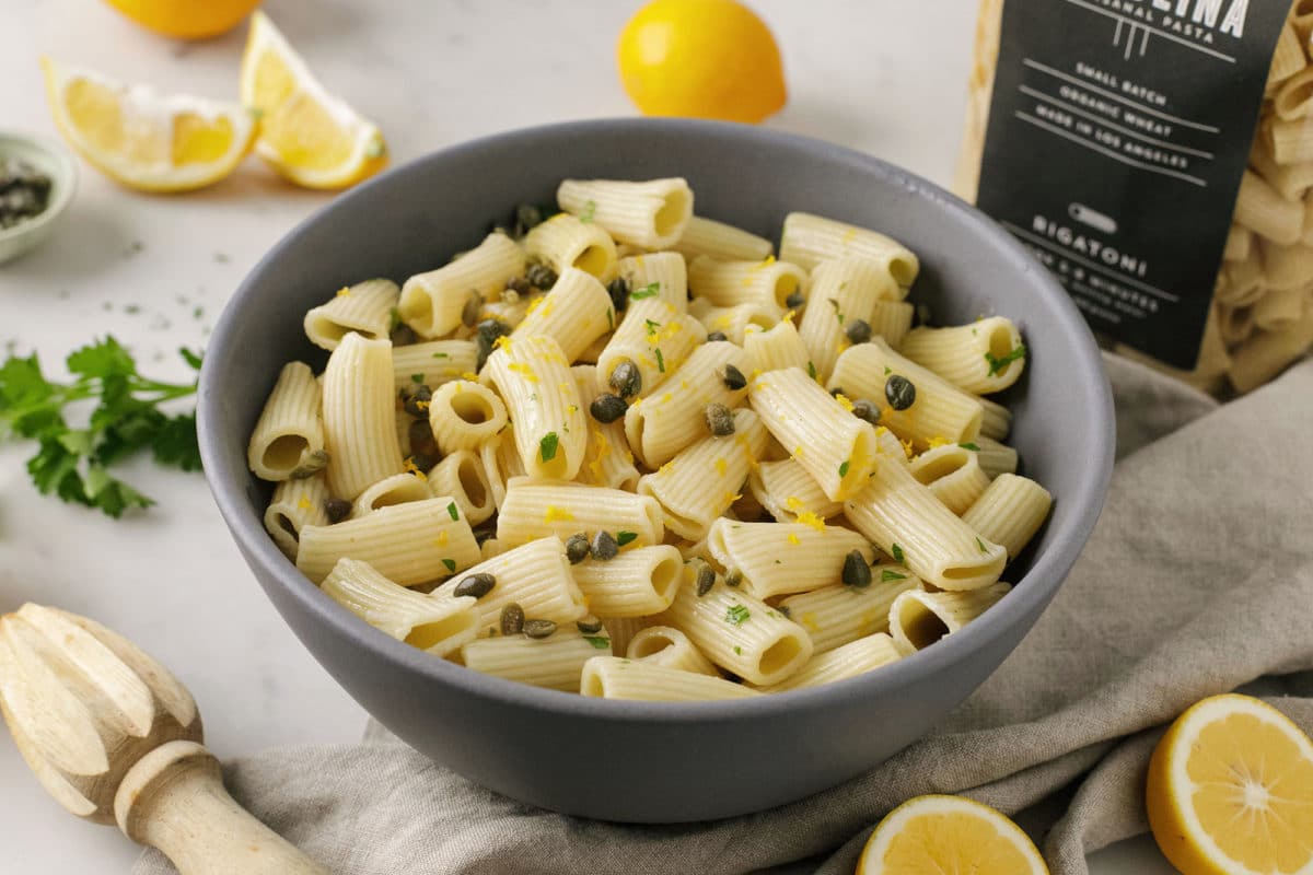 A bowl of rigatoni with herbs and lemon wedges