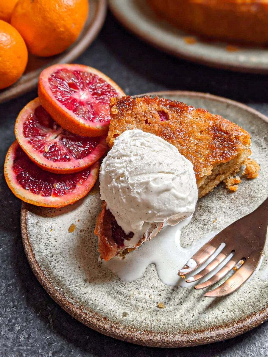 A slice of orange cardamom cake served a la mode with blood orange wheels to the side