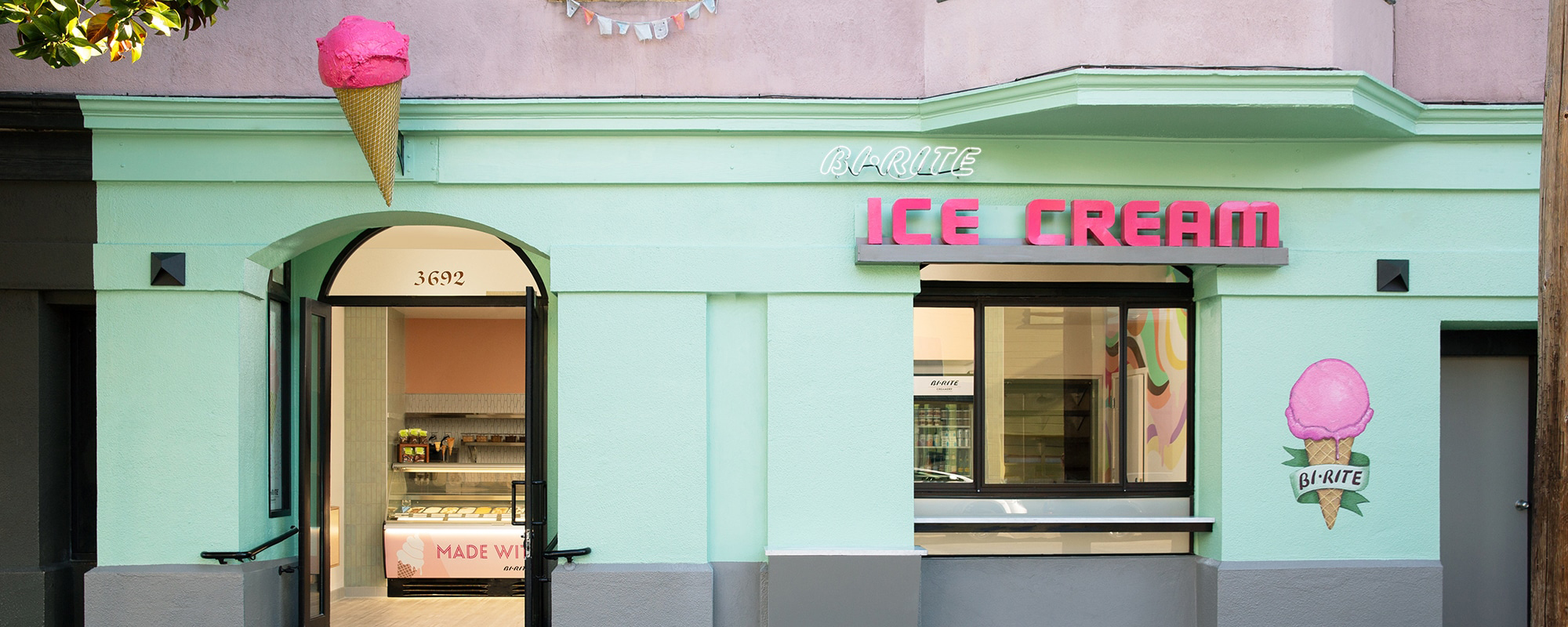 Front of green and pink Creamery, with ice cream cone sculpture above door and mural art on wall