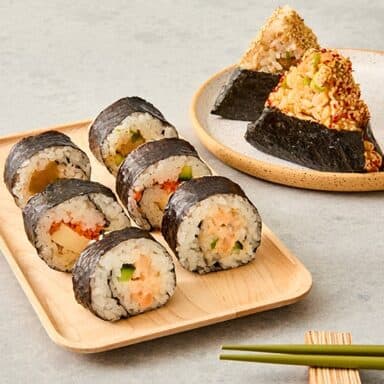 6 Rolls Sushi On Plate Next To 2 Onigiri And Chopsticks On Grey