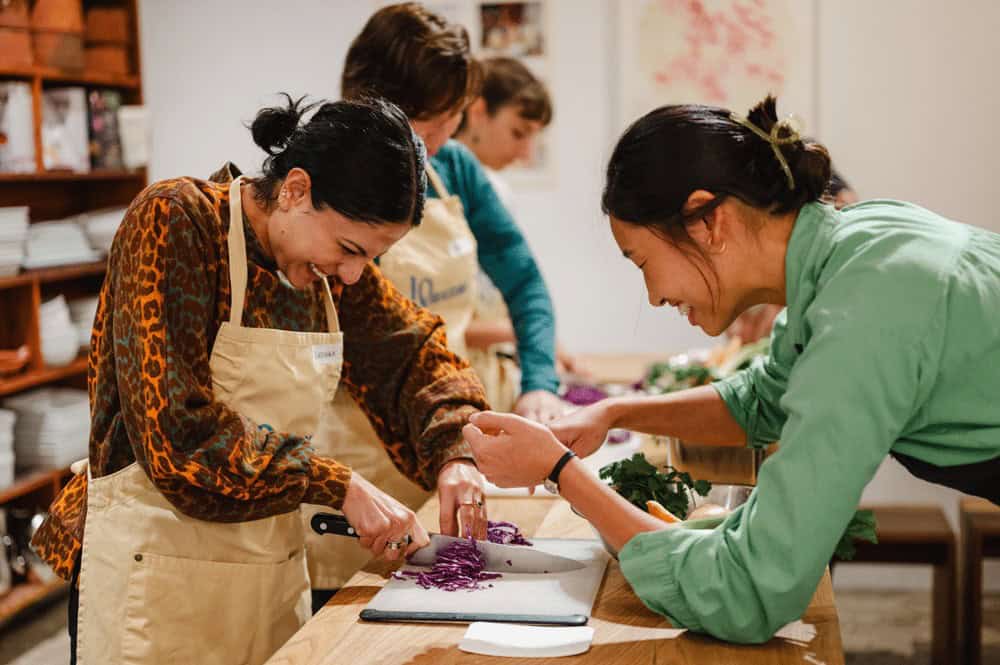 Instructor helps a student chop vegetables during an 18 Reasons cooking class