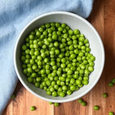 Bowl Of Peas With Scattered Peas On Wood With Blue Napkin Cutting Down Center
