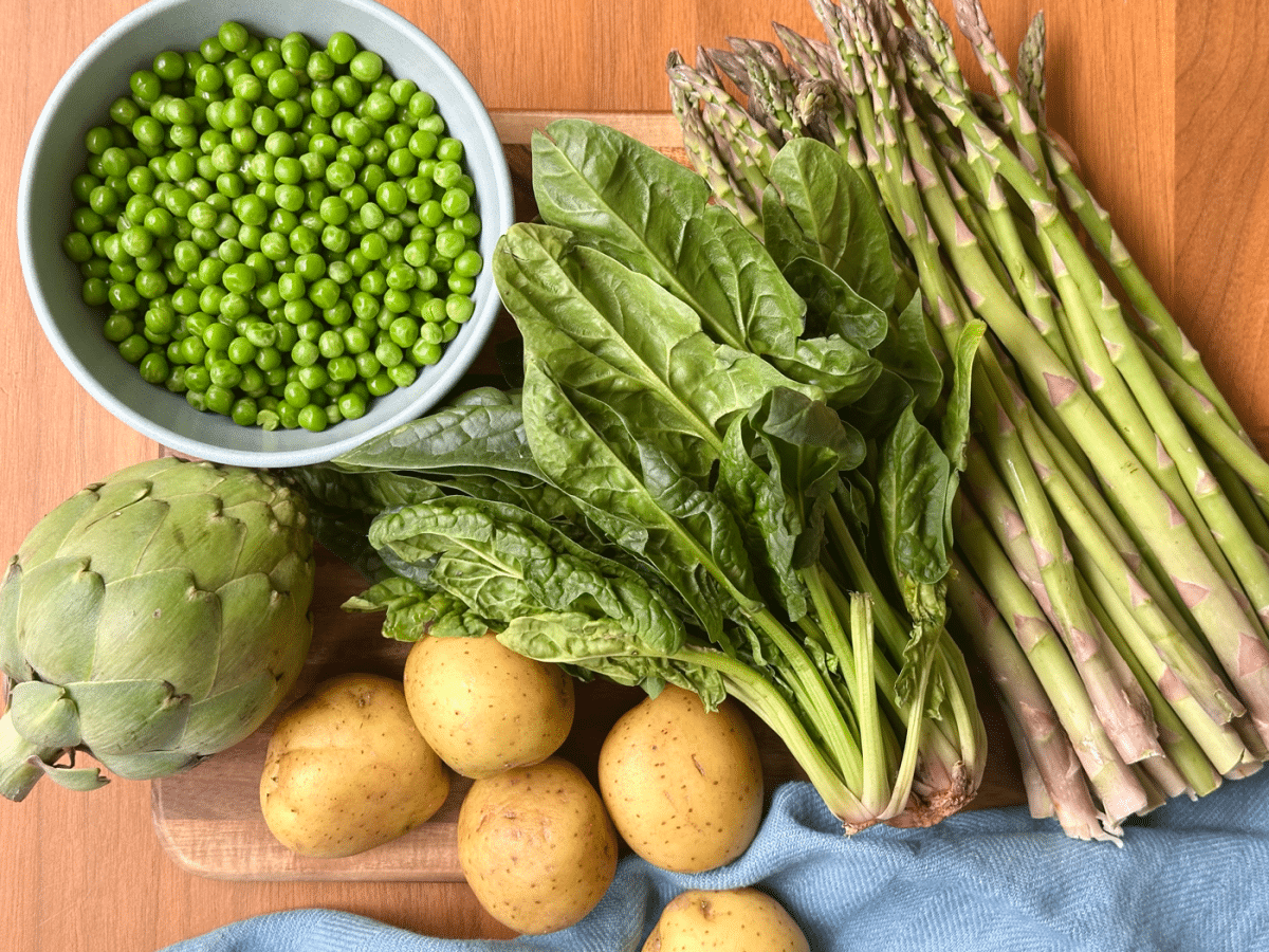 Mis En Place Of Bowl Of Peas Artichoke Golden Potatoes Bunch Of Lettuce Bunch Of Asparagus On Wood Cutting Board With Blue Napkin