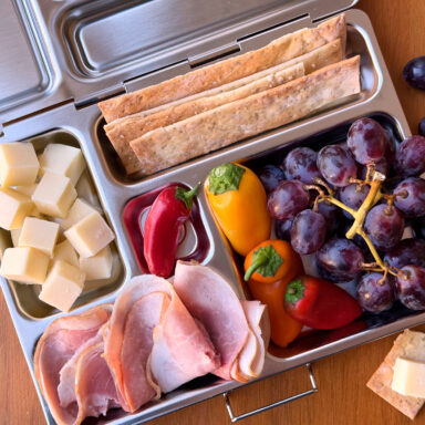 Open Lunch Box Of Cheese Peppers Meats Grapes And Crackers