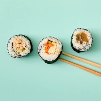 Three Pieces Of Sushi Shot From Above With Chopsticks On Teal Background